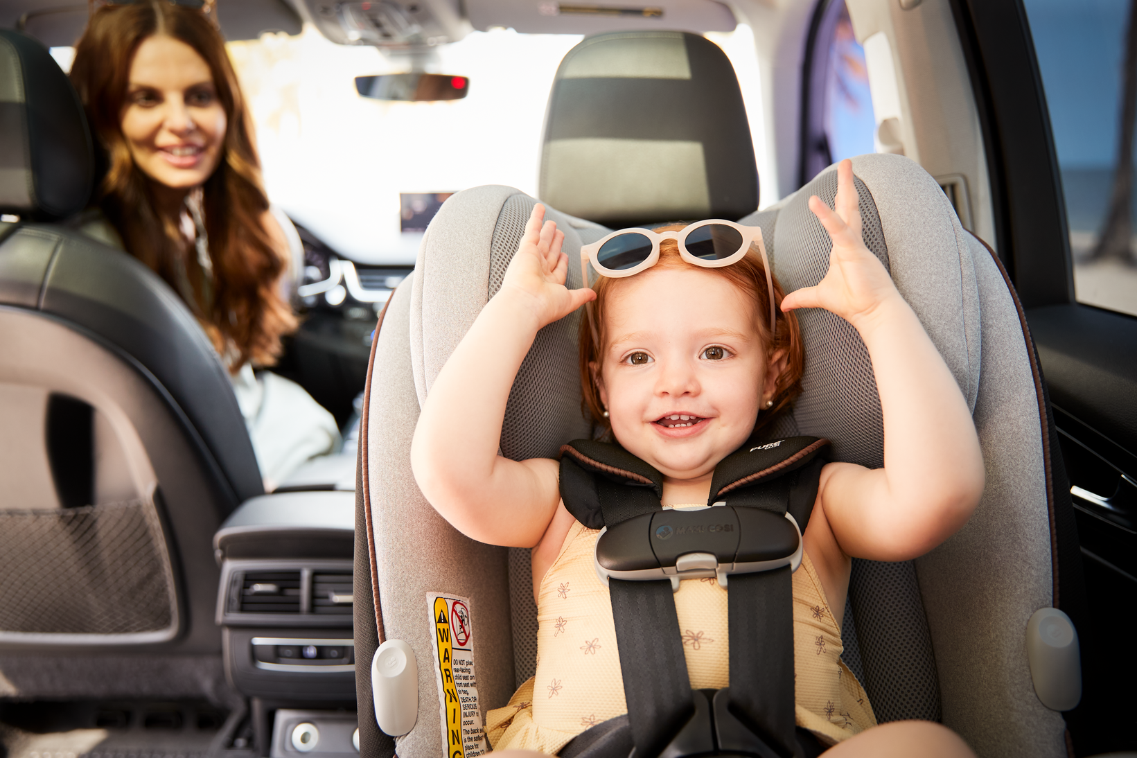 toddler in rear facing car seat wearing sunglasses with mother in background