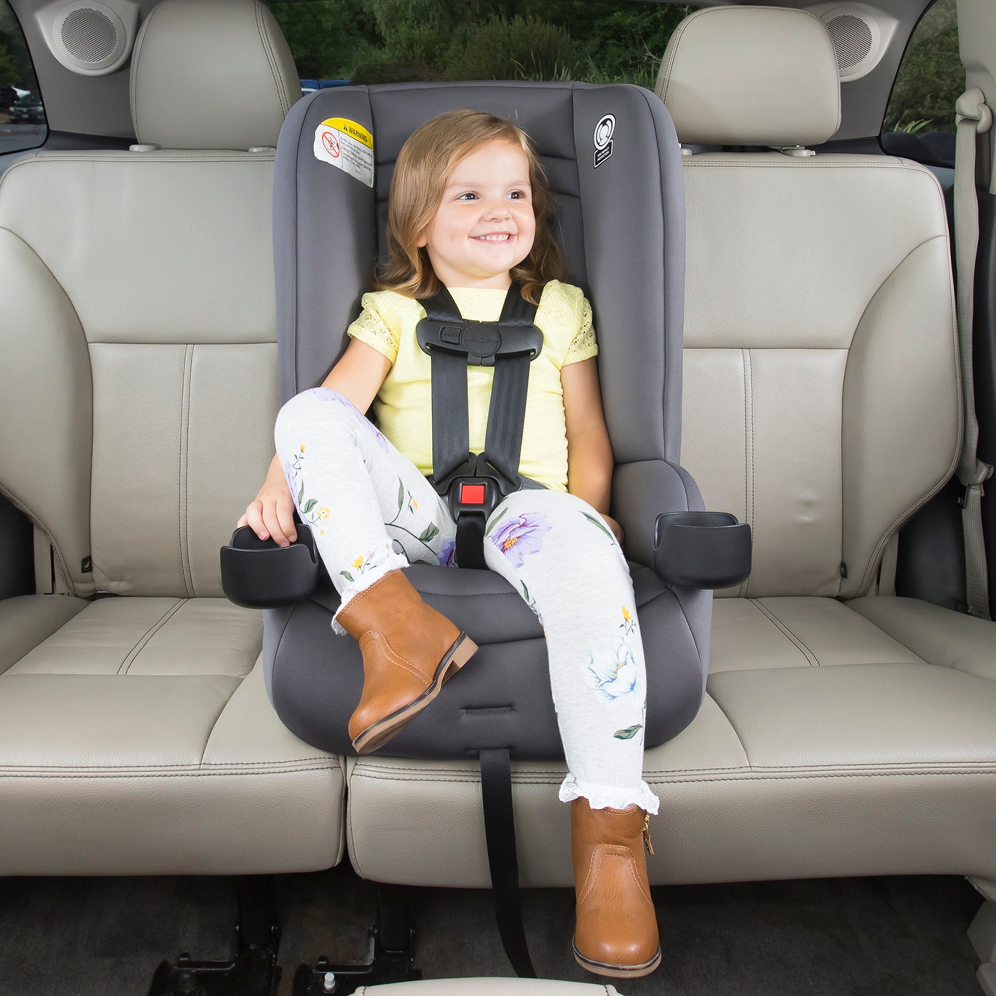toddler in yellow shirt sitting in convertible car seat in car middle seat