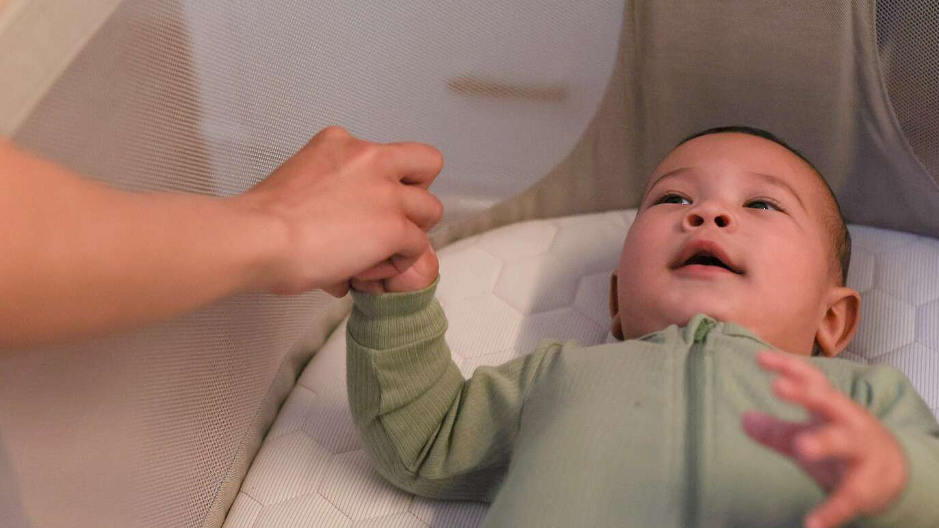 baby in crib with mother holding his hand