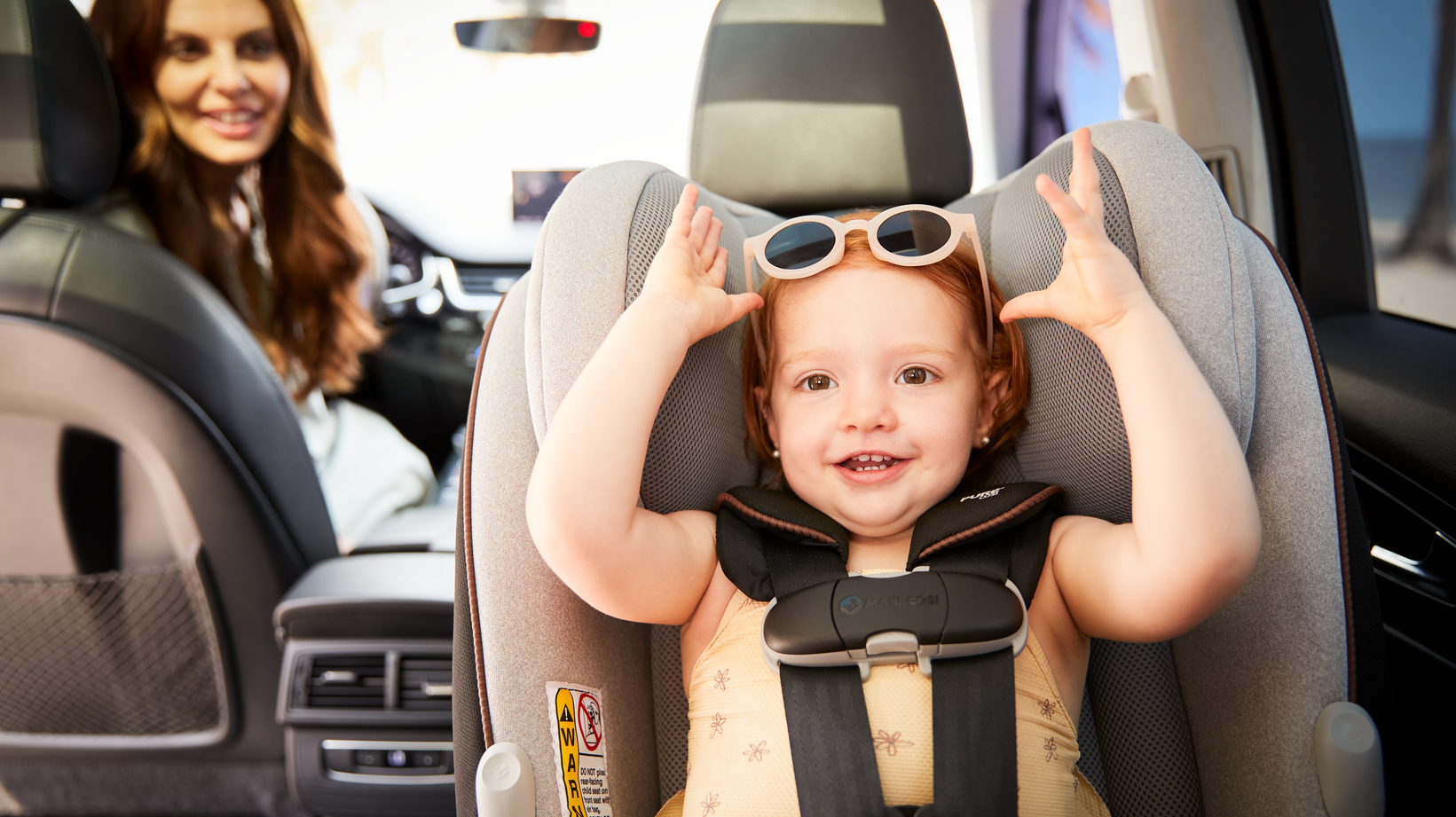 toddler in rear facing car seat wearing sunglasses with mother in background