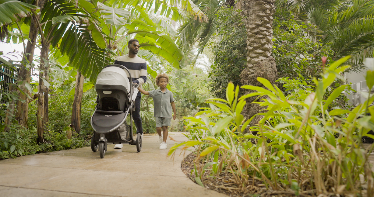 father and son walking with stroller on pathway surrounded by lush greenery