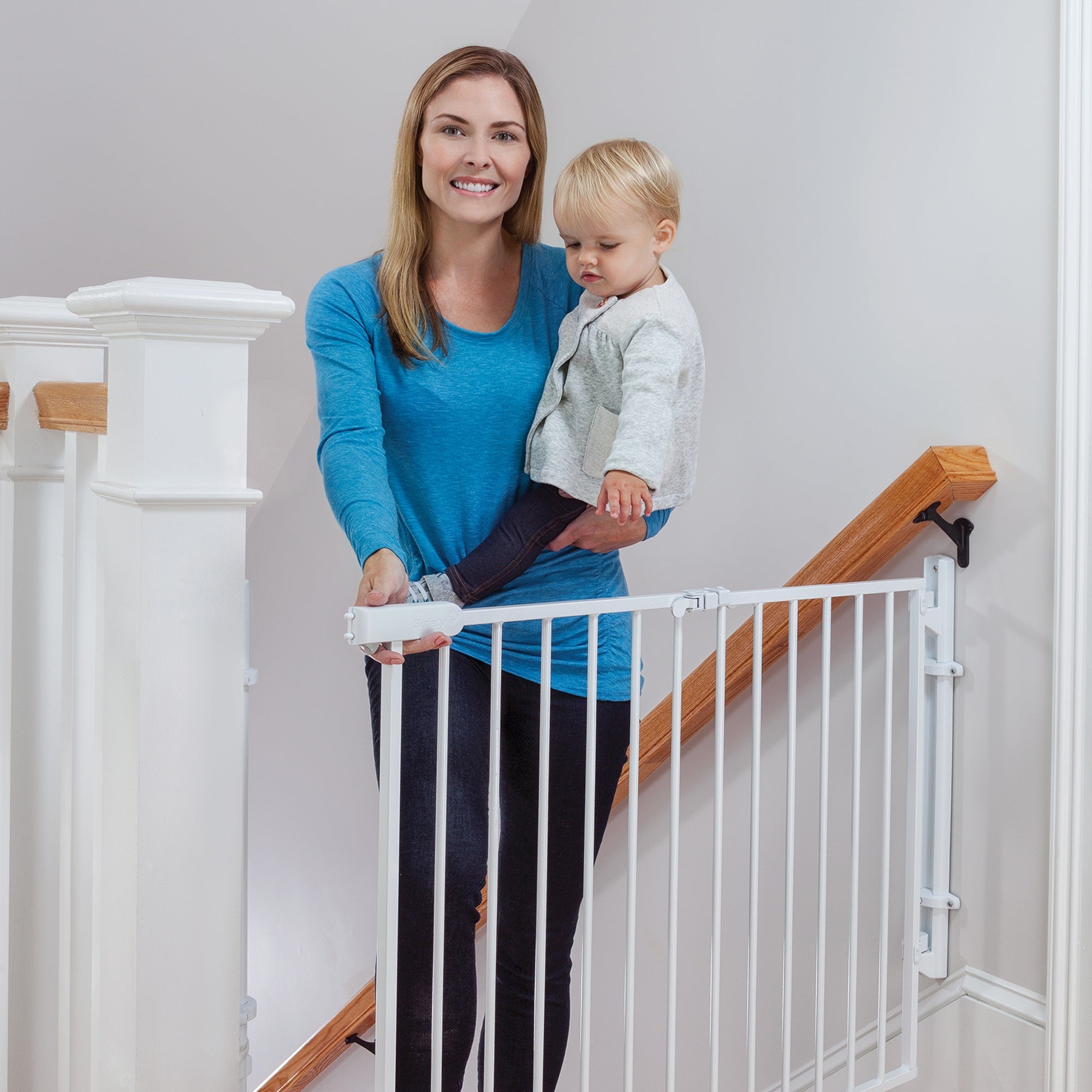 mom wearing blue shirt holding baby at top of stairs opening gate