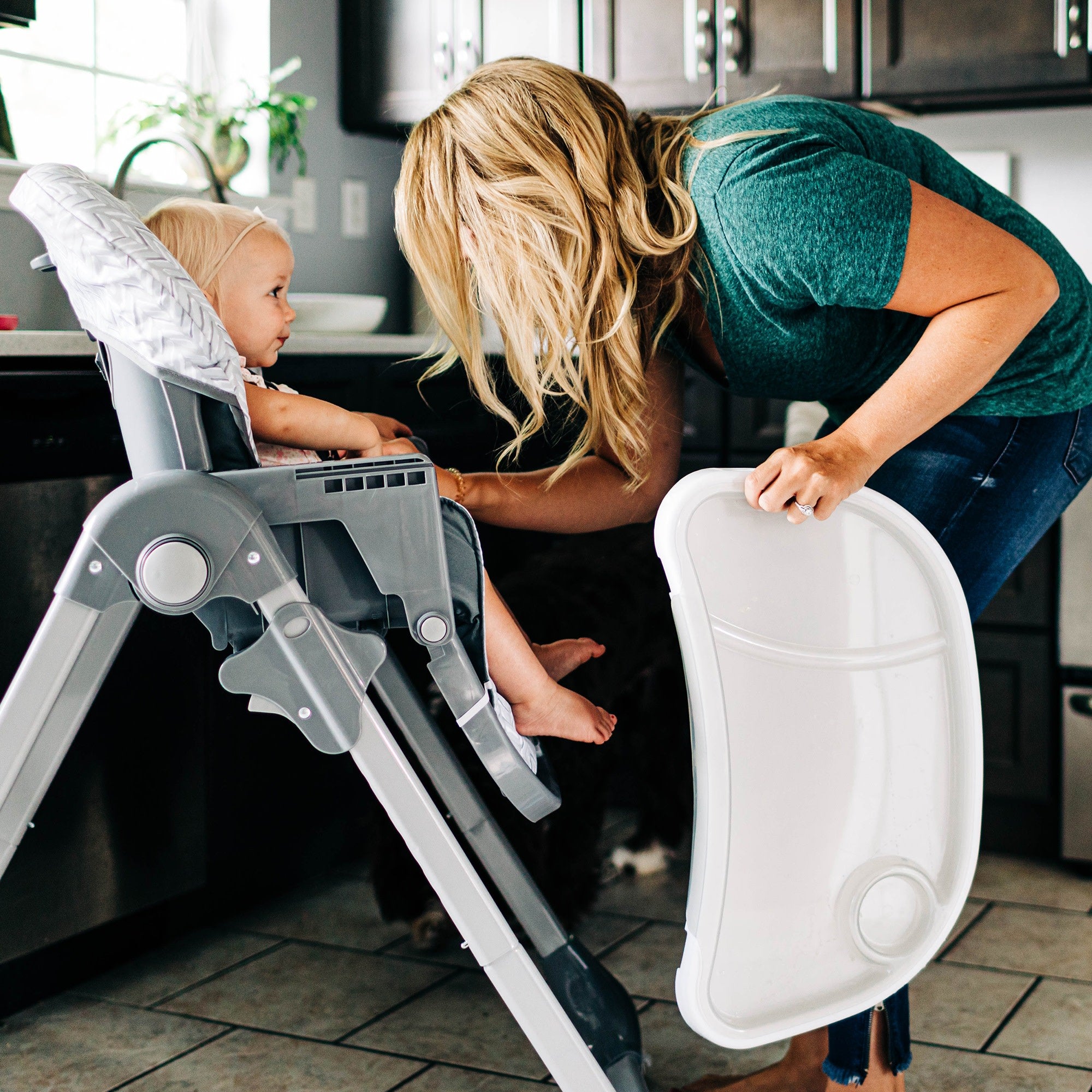 mom holding high chair tray with toddler girl in seat
