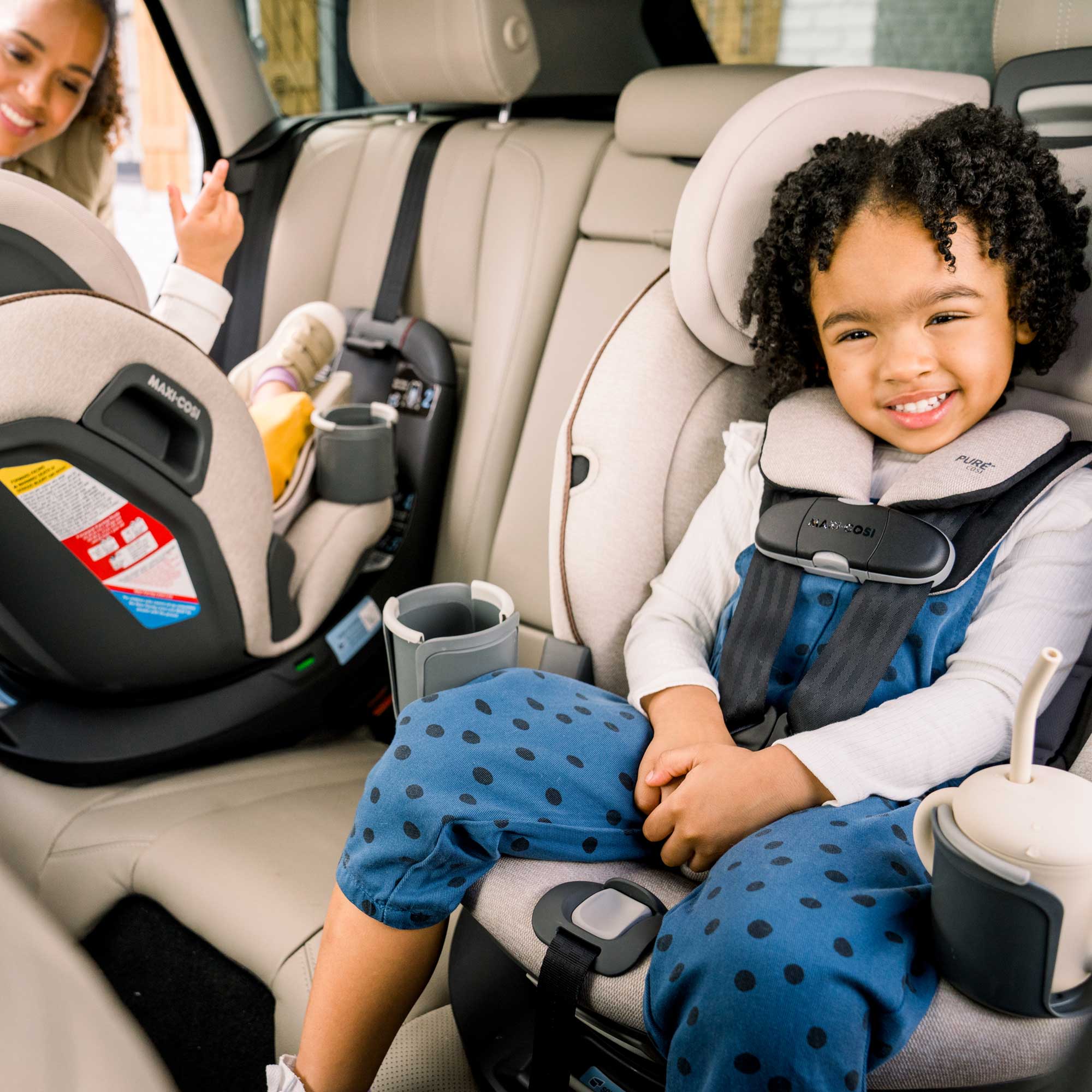 Emme 360™ Rotating All-in-One Convertible Car Seat - two children in front-facing and rear facing Emmes in the car, with mother smiling by their side