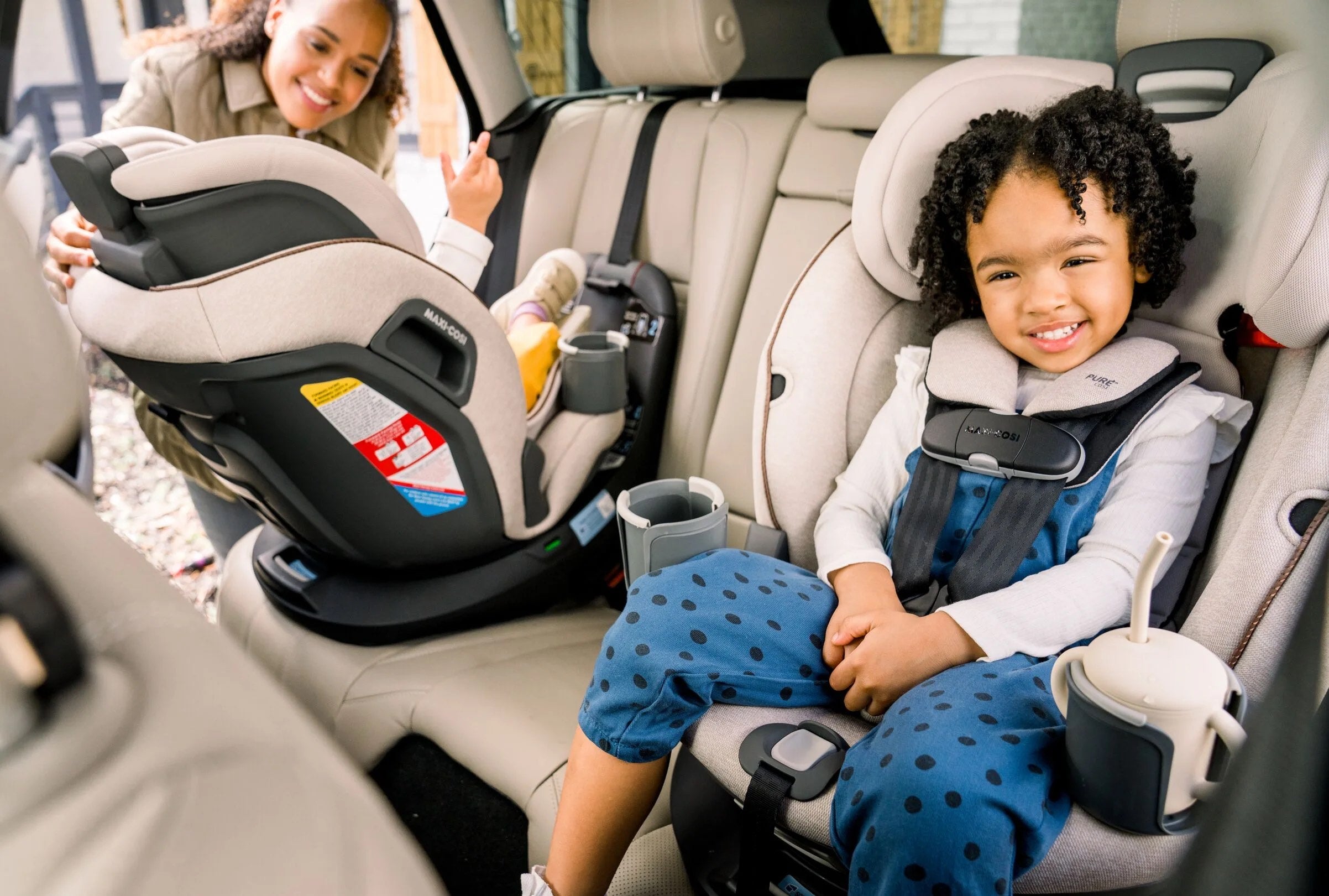 children in back seat of car in two infant car seats with mother adjusting one seat