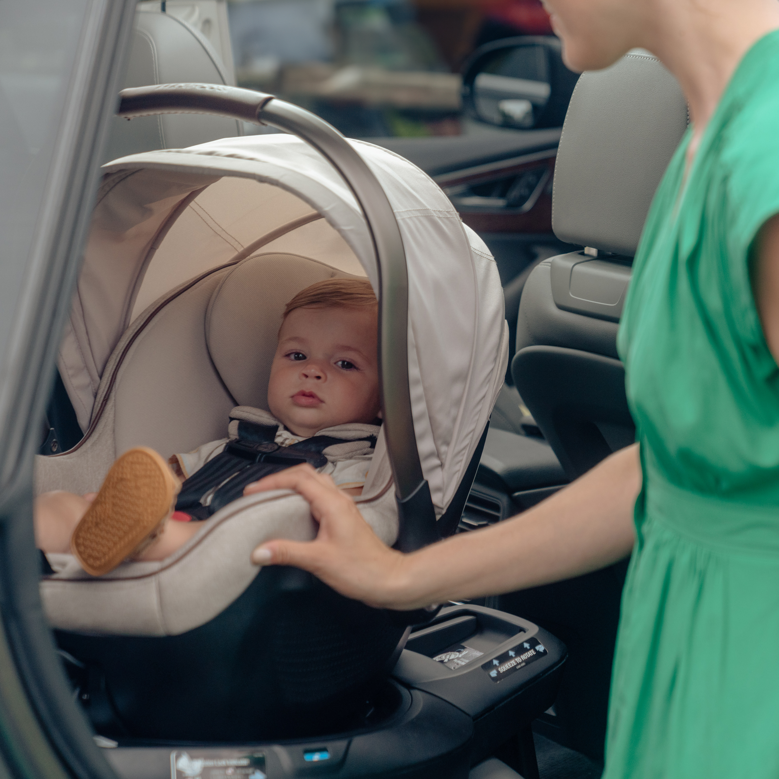 baby sitting in infant car seat in car with mom resting hand on outside of seat