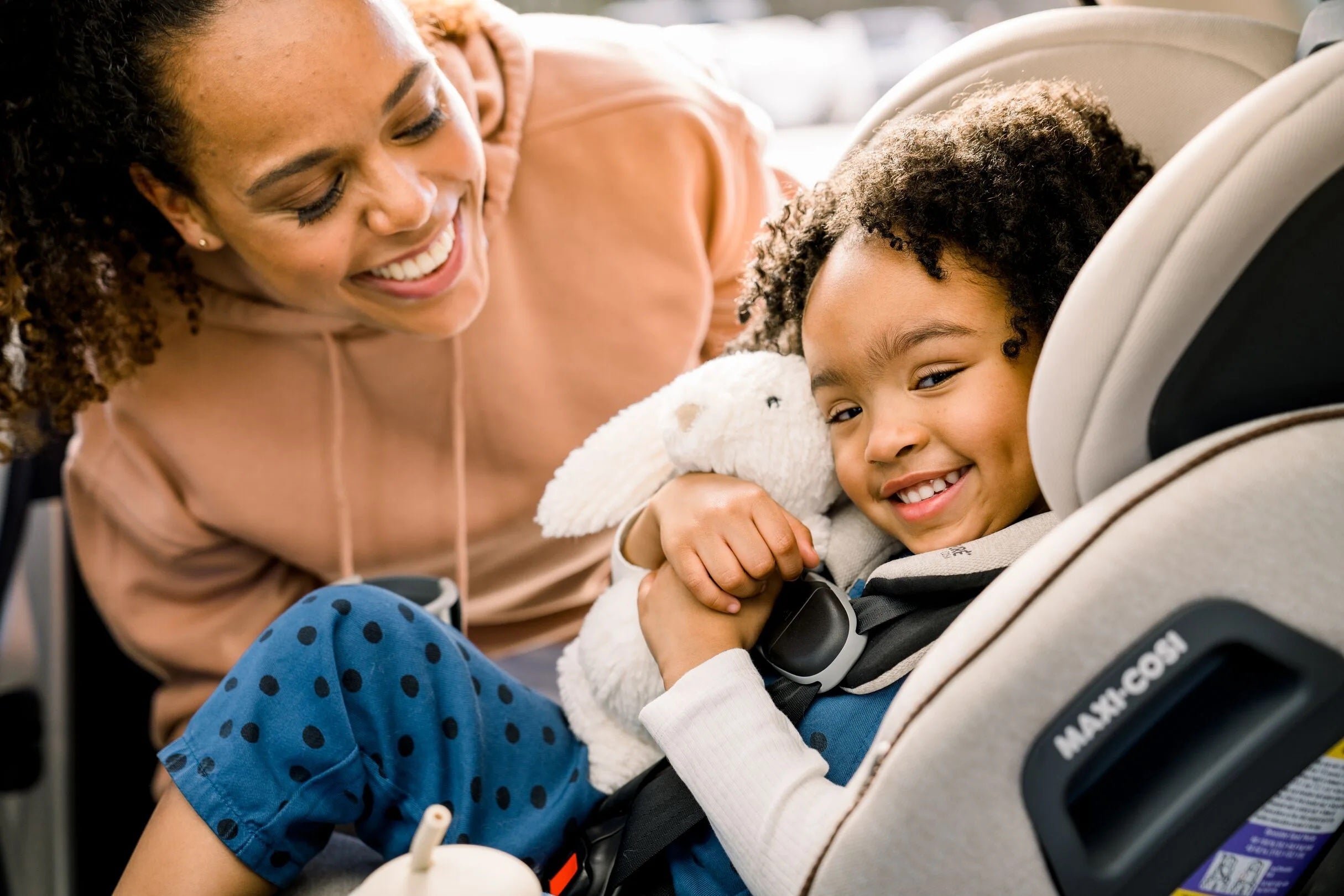 daughter holding bunny stuffed animal in infant car seat with mother smiling by her side