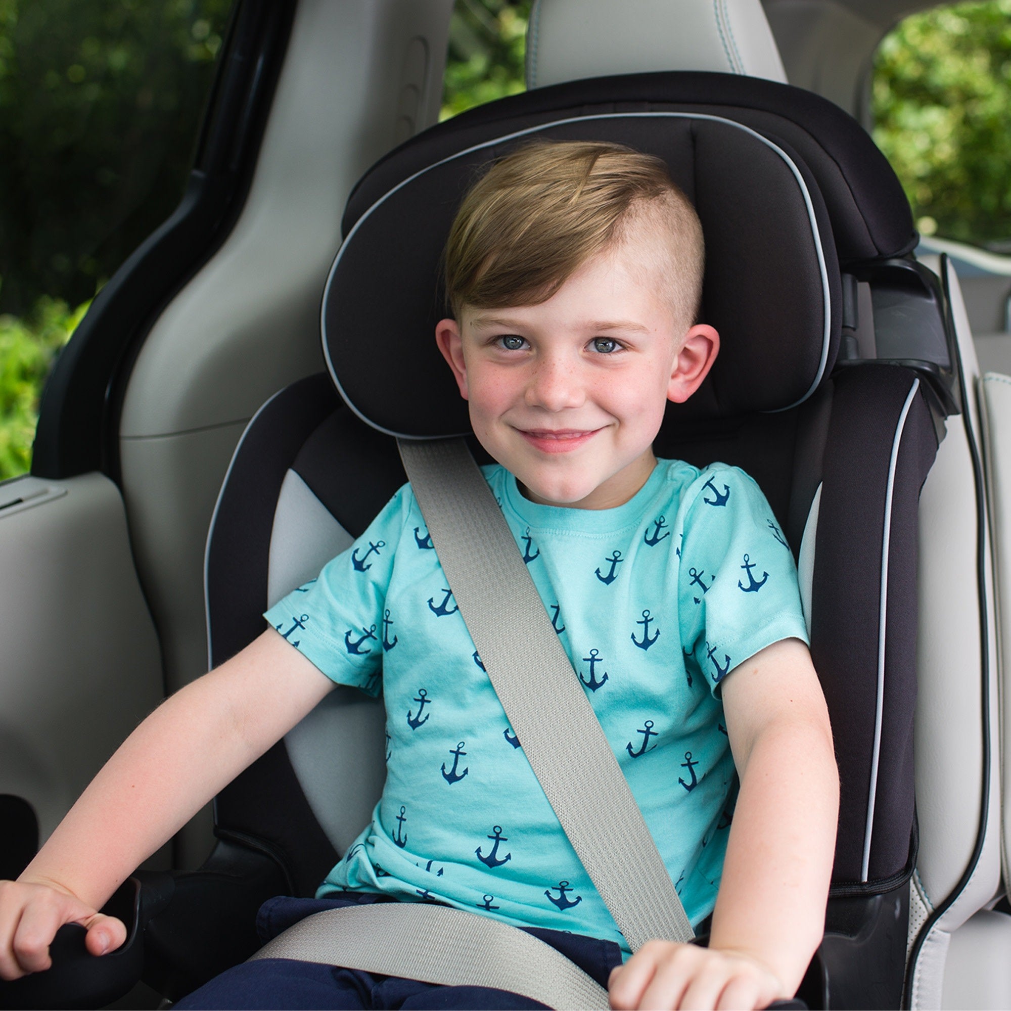 toddler boy in blue shirt with anchors sitting in booster car seat with vehicle belt